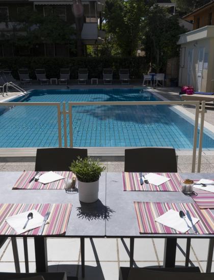 Tavolo apparecchiato vicino a piscina, atmosfera rilassante e soleggiata.
