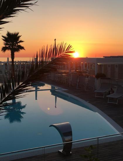 Tramonto dorato su piscina tranquilla, palme e cielo infuocato.