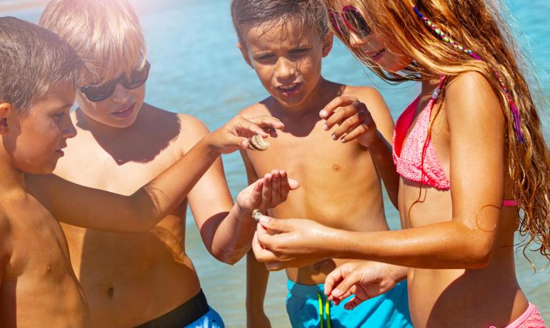 Bambini felici giocano in spiaggia, esplorando conchiglie sotto il sole.