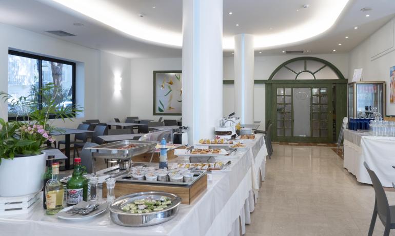 Sala colazione elegante con buffet ricco e atmosfera luminosa.