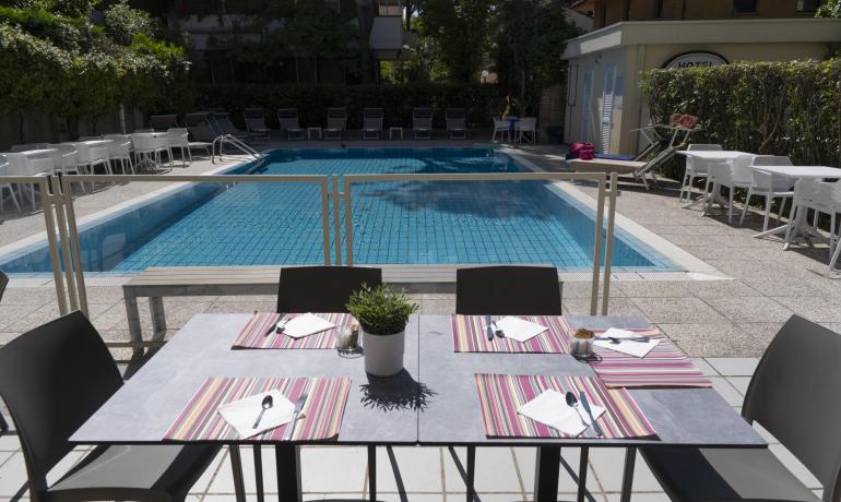 Tavolo apparecchiato vicino a piscina, atmosfera rilassante e soleggiata.