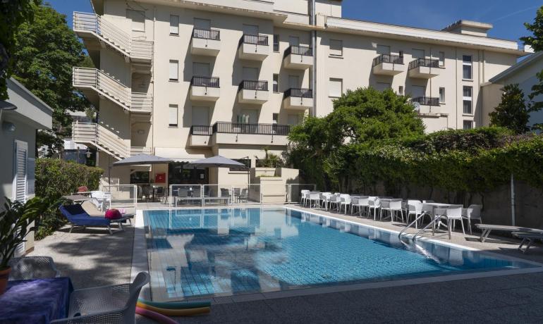 Piscine scintillante près d'un bâtiment moderne, ambiance relaxante et ensoleillée.