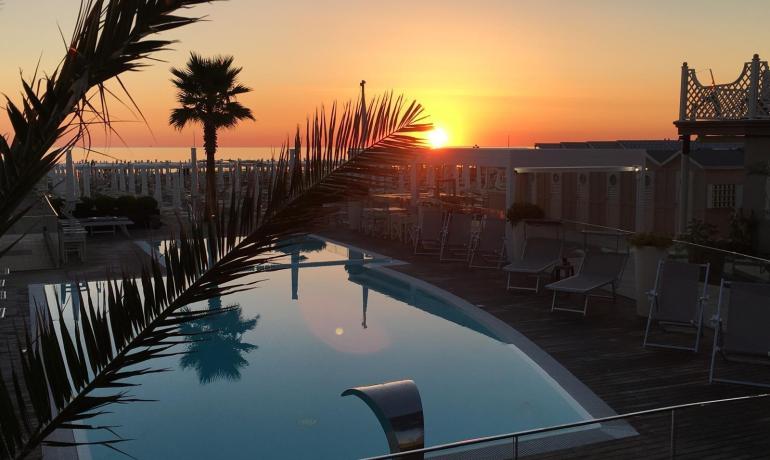 Tramonto dorato su piscina tranquilla, palme e cielo infuocato.