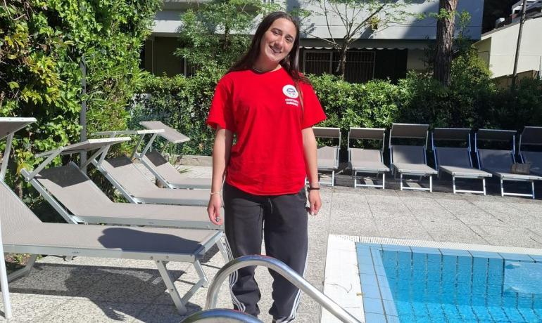 Fille souriante en rouge près d'une piscine, journée ensoleillée et détente.