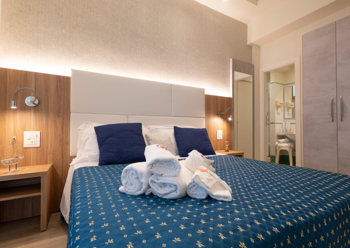 Camera moderna con letto matrimoniale, cuscini blu, asciugamani piegati e arredo elegante.